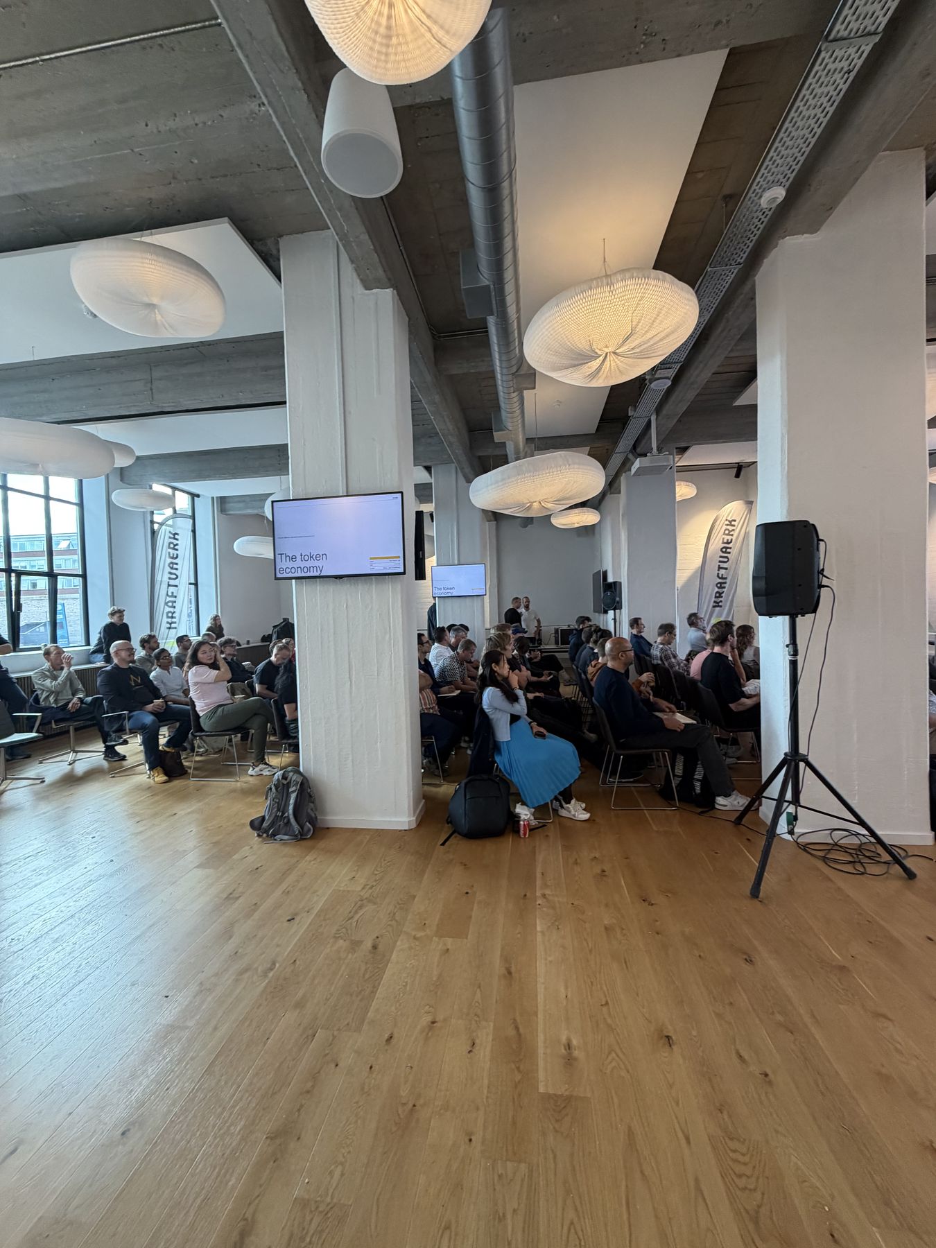 Audiencia en Tech Passion Day 2026, en un espacio industrial en Copenhague, con una pantalla que dice The token economy.